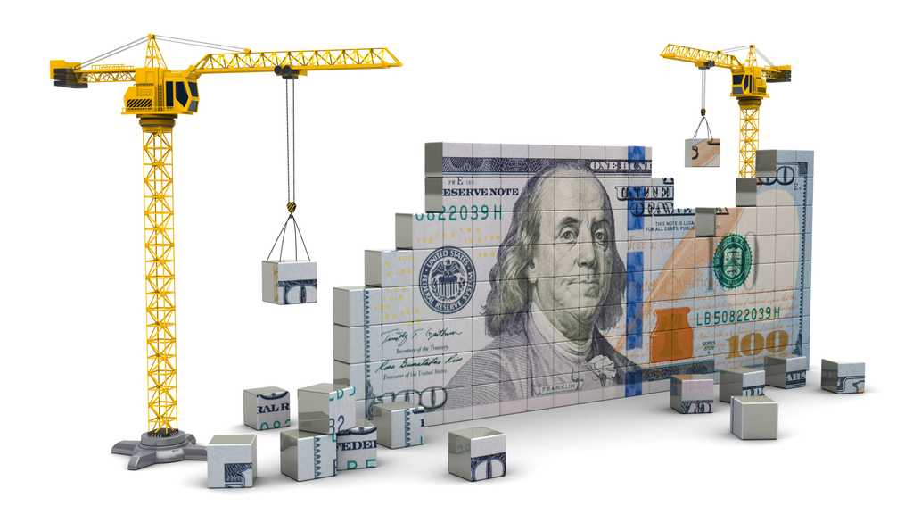 Building blocks being hoisted by cranes that are constructing a one hundred dollar bill